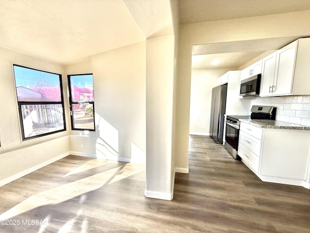 kitchen with white cabinetry, appliances with stainless steel finishes, wood-type flooring, and light stone counters