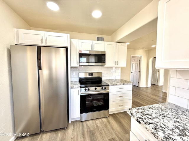 kitchen with tasteful backsplash, white cabinetry, appliances with stainless steel finishes, and light stone counters