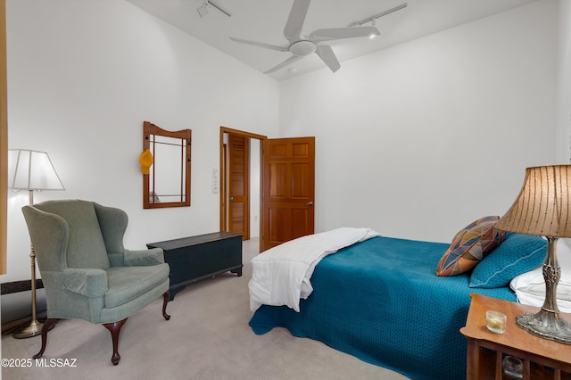 carpeted bedroom with ceiling fan, track lighting, and a high ceiling