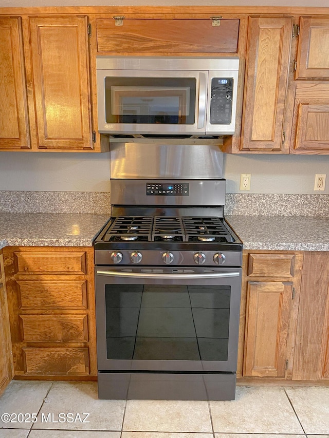 kitchen with light stone counters, appliances with stainless steel finishes, and light tile patterned flooring