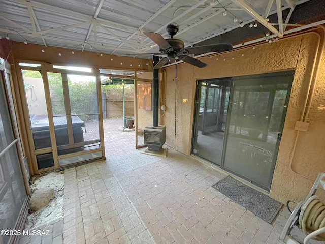 unfurnished sunroom featuring ceiling fan and a wood stove