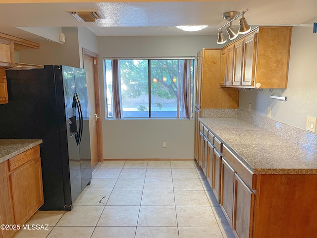 kitchen with black fridge, light tile patterned flooring, and a textured ceiling