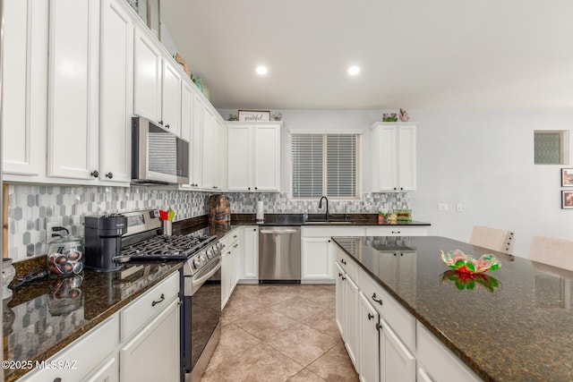 kitchen with sink, appliances with stainless steel finishes, white cabinetry, backsplash, and dark stone countertops