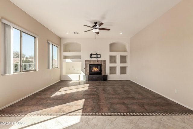 unfurnished living room featuring a tile fireplace, built in features, and ceiling fan