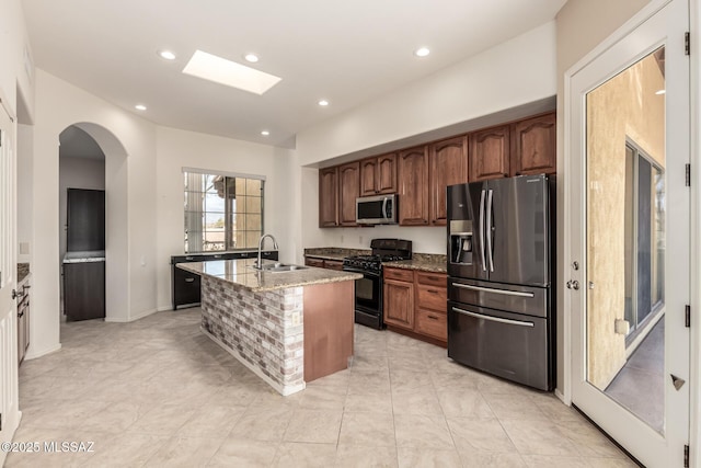 kitchen with light stone counters, appliances with stainless steel finishes, sink, and a kitchen island with sink