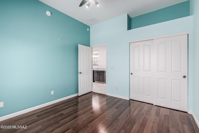 unfurnished bedroom with ceiling fan, dark hardwood / wood-style floors, a closet, and a high ceiling