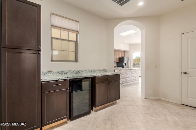 kitchen featuring wine cooler, stainless steel fridge with ice dispenser, light stone counters, and dark brown cabinetry