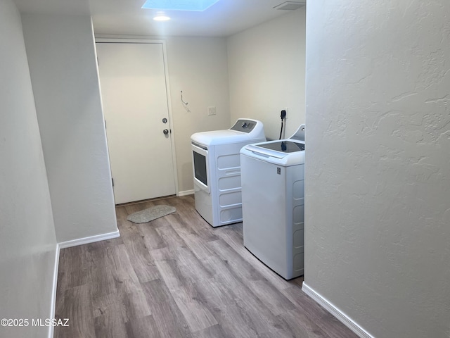 laundry area featuring light wood-type flooring, independent washer and dryer, and a skylight