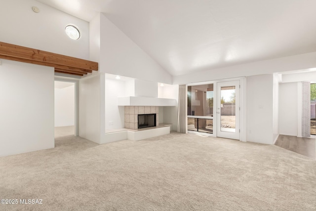 unfurnished living room featuring high vaulted ceiling, light colored carpet, and a tile fireplace