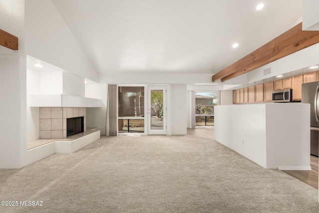 unfurnished living room with light carpet, a tile fireplace, and vaulted ceiling with beams