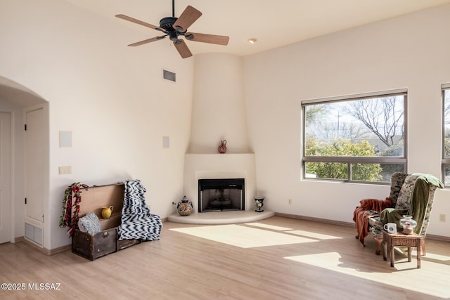 living area featuring ceiling fan, a large fireplace, a high ceiling, and light wood-type flooring