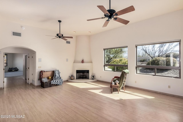 sitting room featuring ceiling fan, a large fireplace, a towering ceiling, and light wood-type flooring