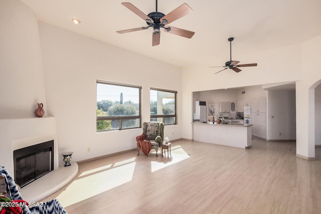 living room featuring a high ceiling, ceiling fan, and light wood-type flooring