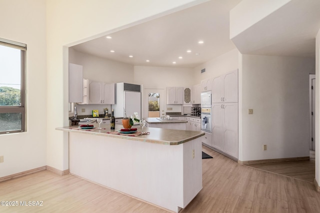 kitchen with sink, white cabinets, built in appliances, kitchen peninsula, and light wood-type flooring