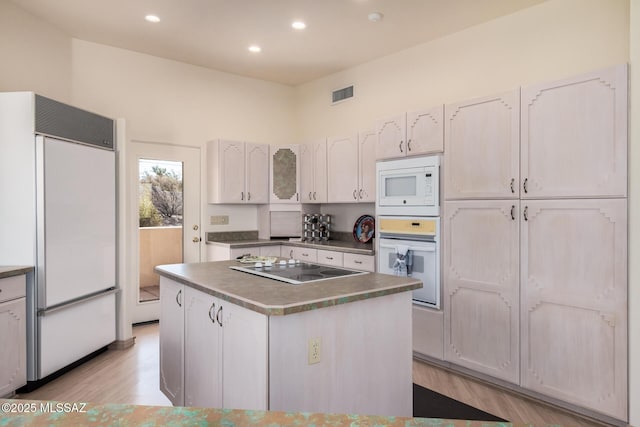 kitchen featuring a kitchen island, built in appliances, white cabinets, and light wood-type flooring