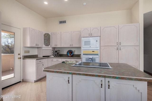 kitchen with white cabinetry, white appliances, light hardwood / wood-style floors, and a center island