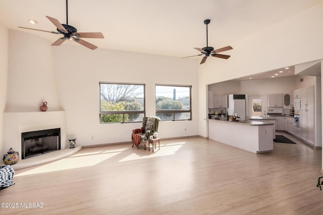 unfurnished living room with ceiling fan, a large fireplace, high vaulted ceiling, and light hardwood / wood-style flooring