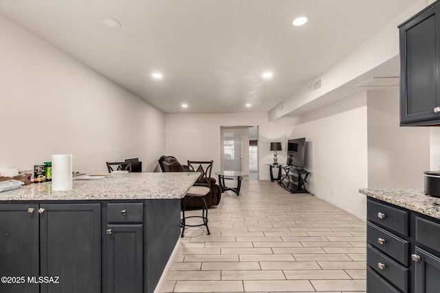 kitchen featuring a breakfast bar, kitchen peninsula, and light stone countertops