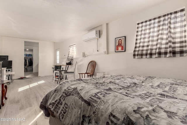 bedroom with a wall mounted air conditioner, a walk in closet, and light hardwood / wood-style flooring