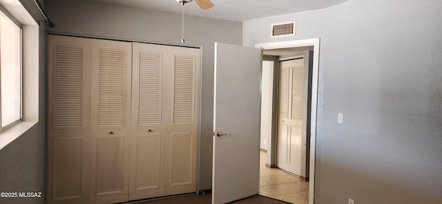 unfurnished bedroom with ceiling fan, light tile patterned floors, a closet, and a textured ceiling