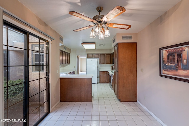 kitchen with light tile patterned flooring, range, kitchen peninsula, white fridge, and ceiling fan