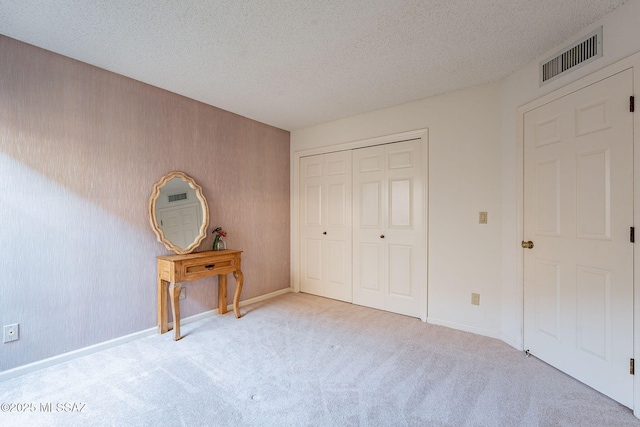 unfurnished bedroom with light colored carpet, a closet, and a textured ceiling