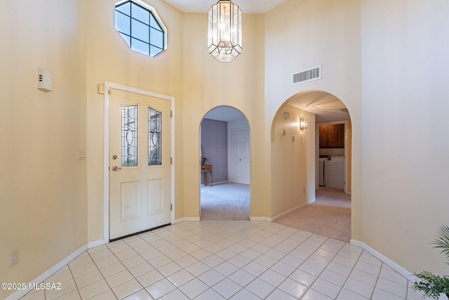 foyer entrance featuring washer / clothes dryer, a towering ceiling, light colored carpet, and a chandelier