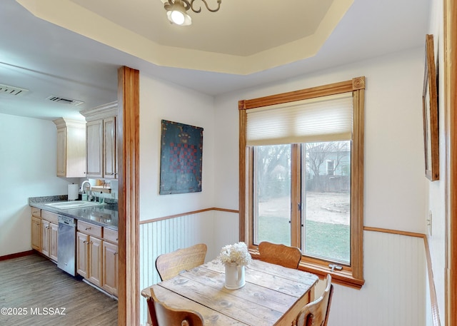 dining room with a tray ceiling, sink, and light hardwood / wood-style flooring