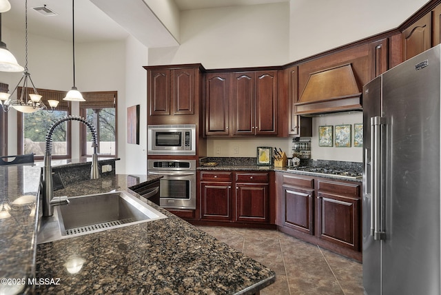 kitchen featuring custom exhaust hood, decorative light fixtures, visible vents, appliances with stainless steel finishes, and a sink