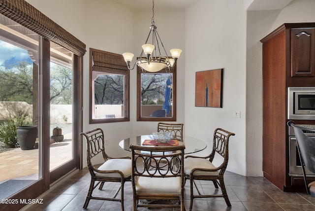 dining room with dark tile patterned floors, a towering ceiling, and an inviting chandelier