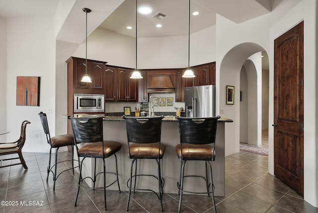 kitchen featuring a breakfast bar, a high ceiling, premium range hood, appliances with stainless steel finishes, and arched walkways