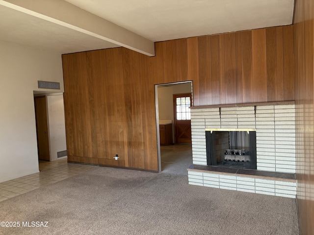 unfurnished living room featuring beam ceiling, a brick fireplace, carpet flooring, and wooden walls