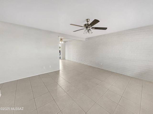 tiled spare room featuring ceiling fan and brick wall