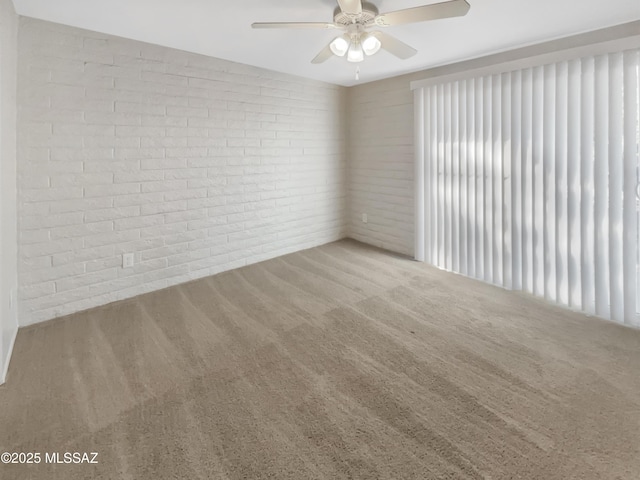 carpeted empty room with ceiling fan and brick wall