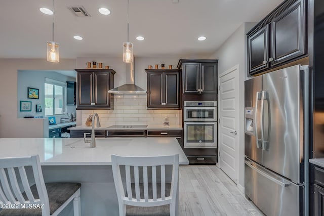 kitchen with wall chimney exhaust hood, appliances with stainless steel finishes, decorative light fixtures, and a breakfast bar area