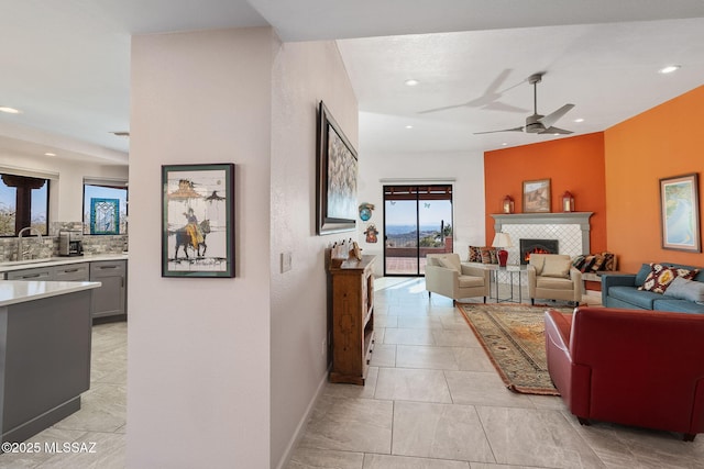 living room featuring ceiling fan, a tiled fireplace, and sink