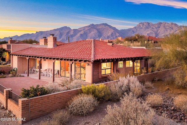 back house at dusk with a mountain view and a patio