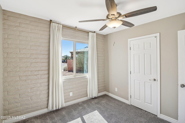 unfurnished bedroom with baseboards, carpet floors, brick wall, and a ceiling fan