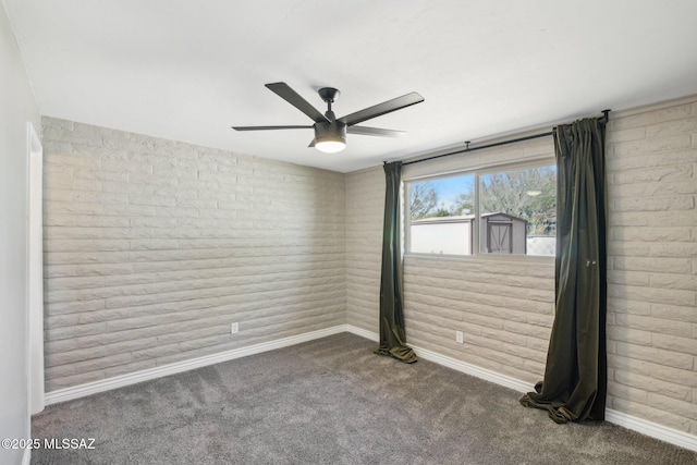 carpeted spare room featuring baseboards, a ceiling fan, and brick wall