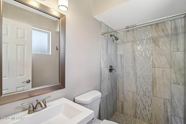 bathroom featuring a tile shower, a sink, and toilet