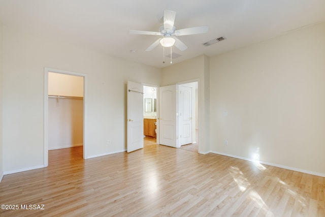 unfurnished bedroom with a closet, a walk in closet, ceiling fan, and light hardwood / wood-style flooring