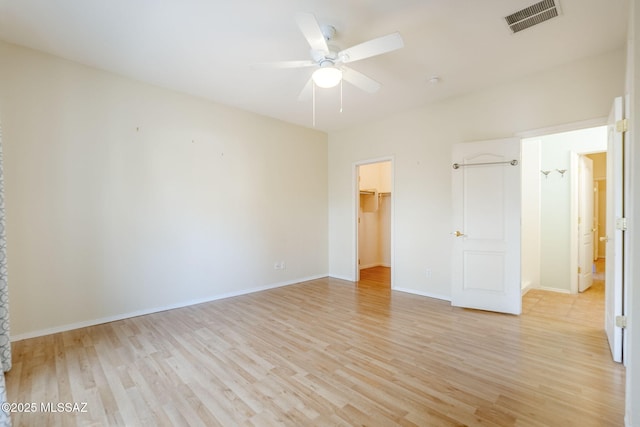 unfurnished bedroom featuring ceiling fan, a walk in closet, a closet, and light hardwood / wood-style flooring