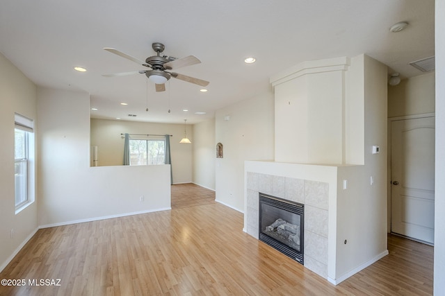 unfurnished living room with ceiling fan, a fireplace, and light wood-type flooring