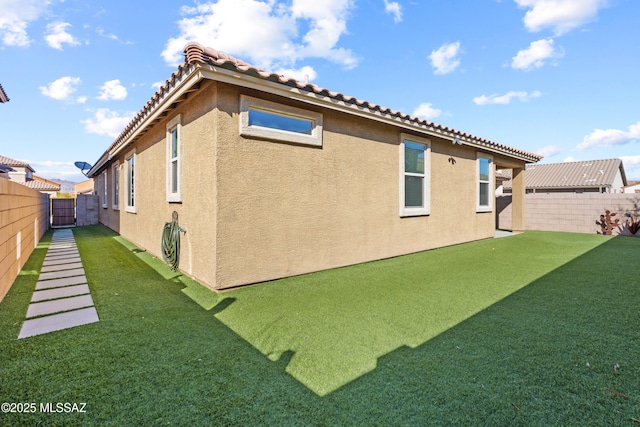 view of side of home with a fenced backyard, a tile roof, a lawn, and stucco siding