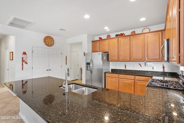 kitchen with stainless steel appliances, visible vents, light tile patterned flooring, a sink, and dark stone countertops