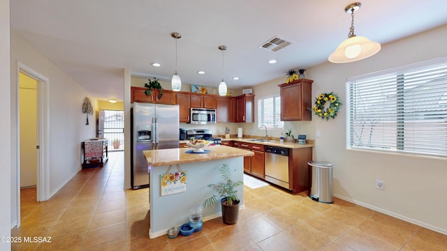 kitchen featuring pendant lighting, sink, light tile patterned floors, appliances with stainless steel finishes, and a center island