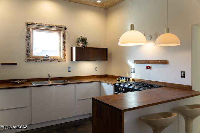 kitchen featuring butcher block counters, sink, range, pendant lighting, and white cabinets