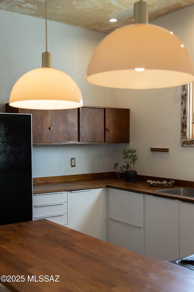 kitchen featuring white cabinetry, decorative light fixtures, and black fridge