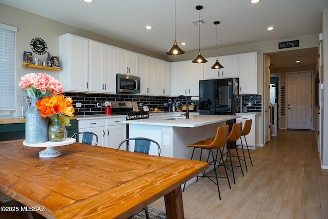 kitchen with appliances with stainless steel finishes, a kitchen island with sink, sink, and white cabinets