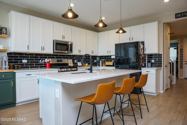 kitchen featuring sink, white cabinetry, light hardwood / wood-style flooring, appliances with stainless steel finishes, and an island with sink